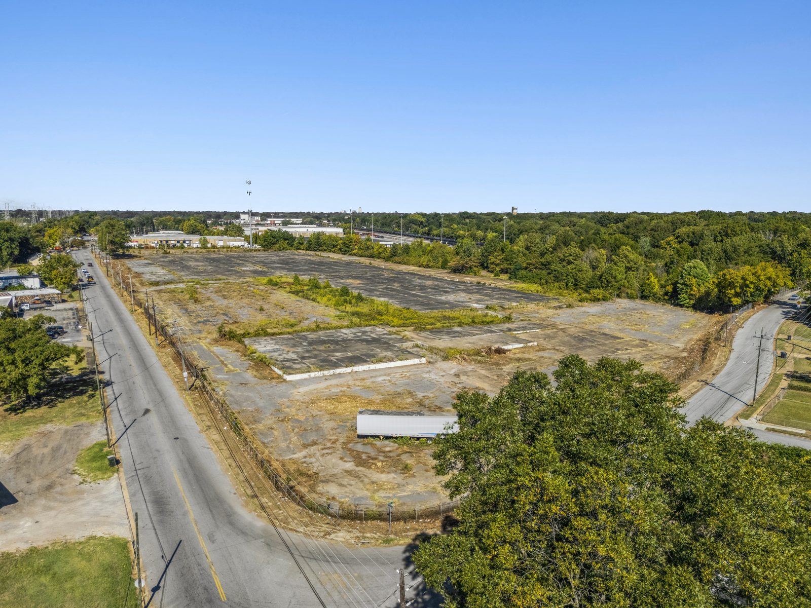 Aerial of the site from its corner, with the street along the left edge, a fence line around the pad and a trailer parked on it.