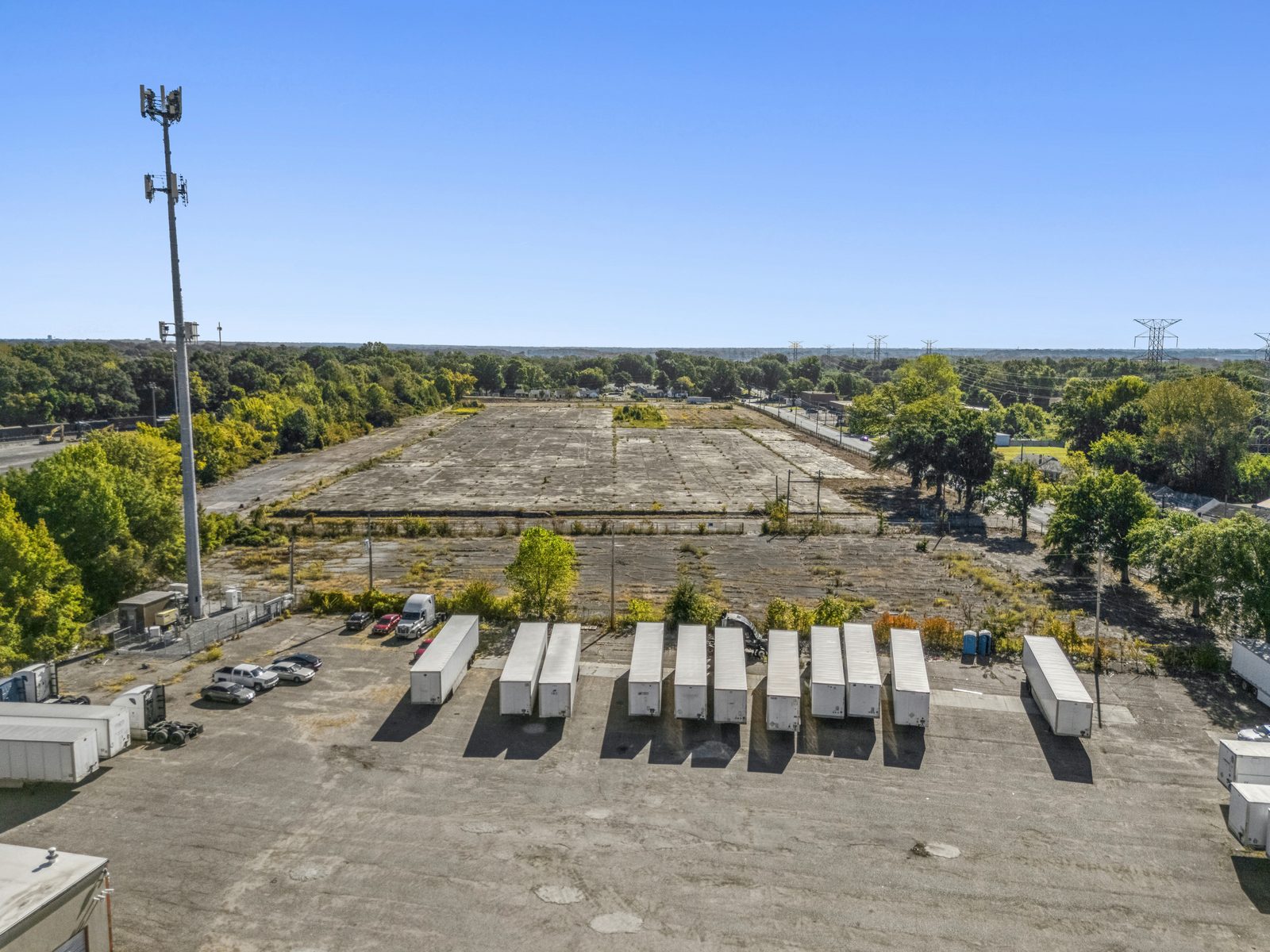 Aerial from above a trailer parking lot, looking across to the concrete pad, with a cell tower at left.