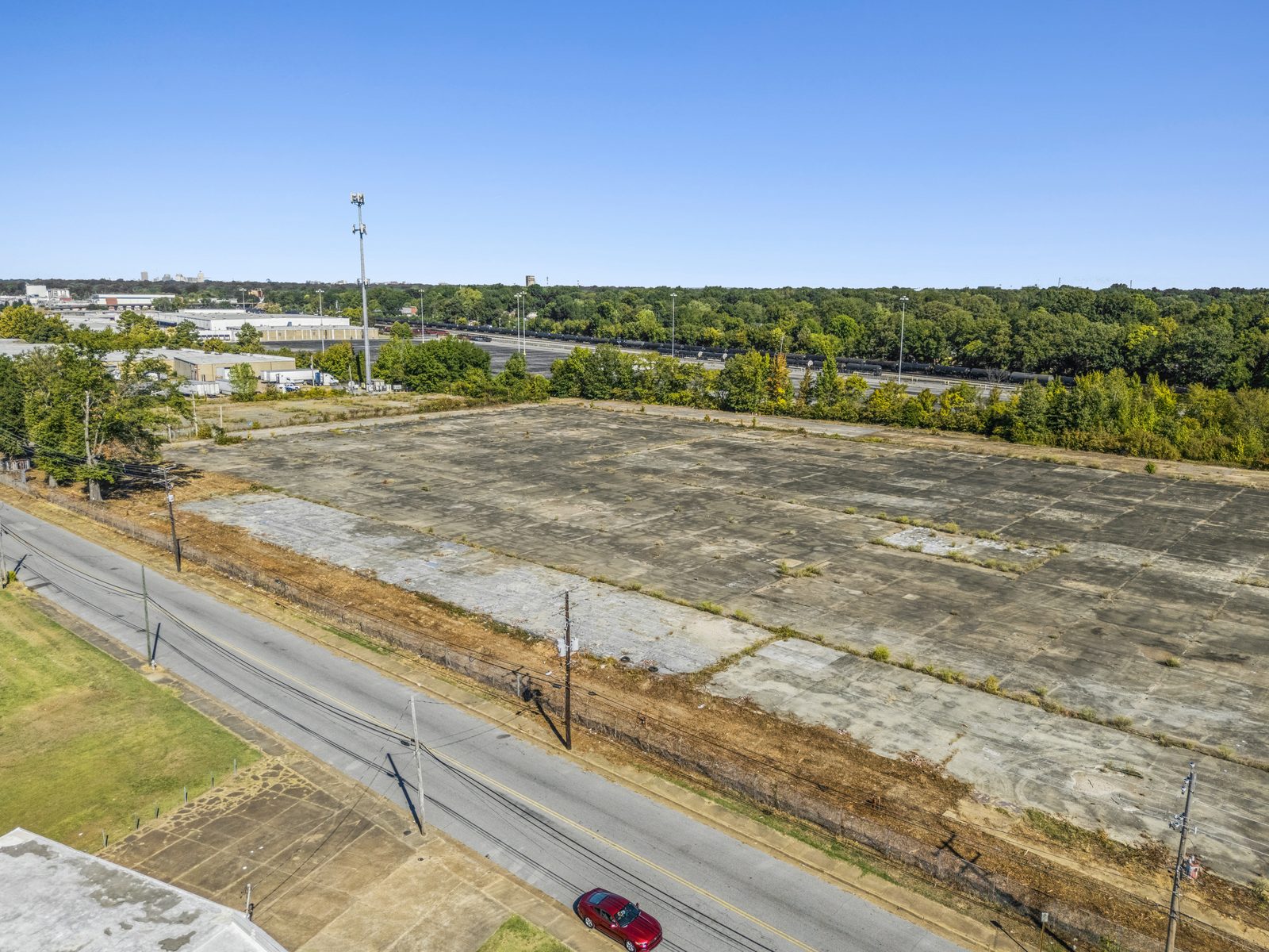 High aerial along the street beside the site, with the concrete pad filling the right side and the interstate behind the trees.