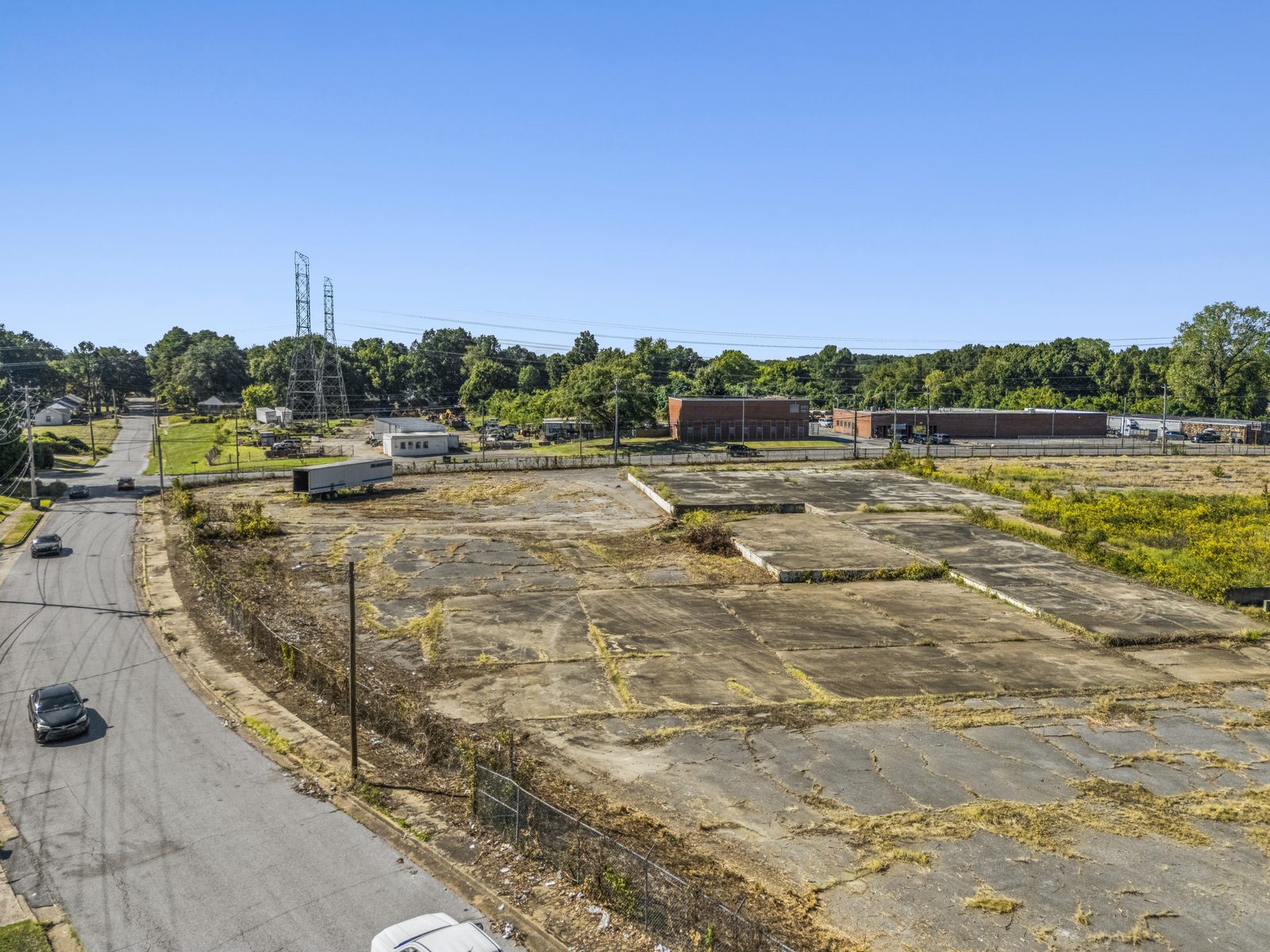 Aerial along the street on the left, looking over the fence onto the concrete slabs, with power lines and brick buildings beyond.