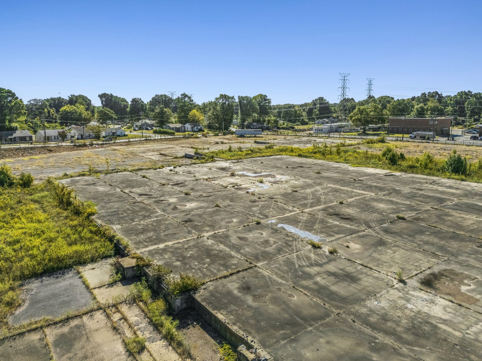 Low aerial of a concrete slab and the remains of an old foundation, with houses and power lines past the site.