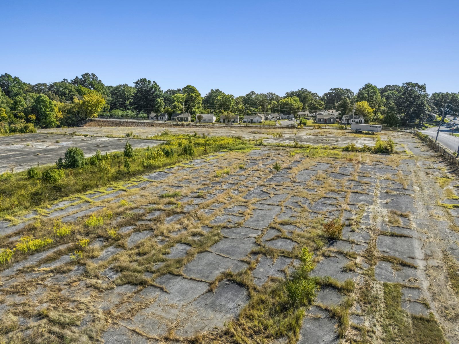 Low aerial of broken concrete slabs with grass in the joints, and the street along the right edge.