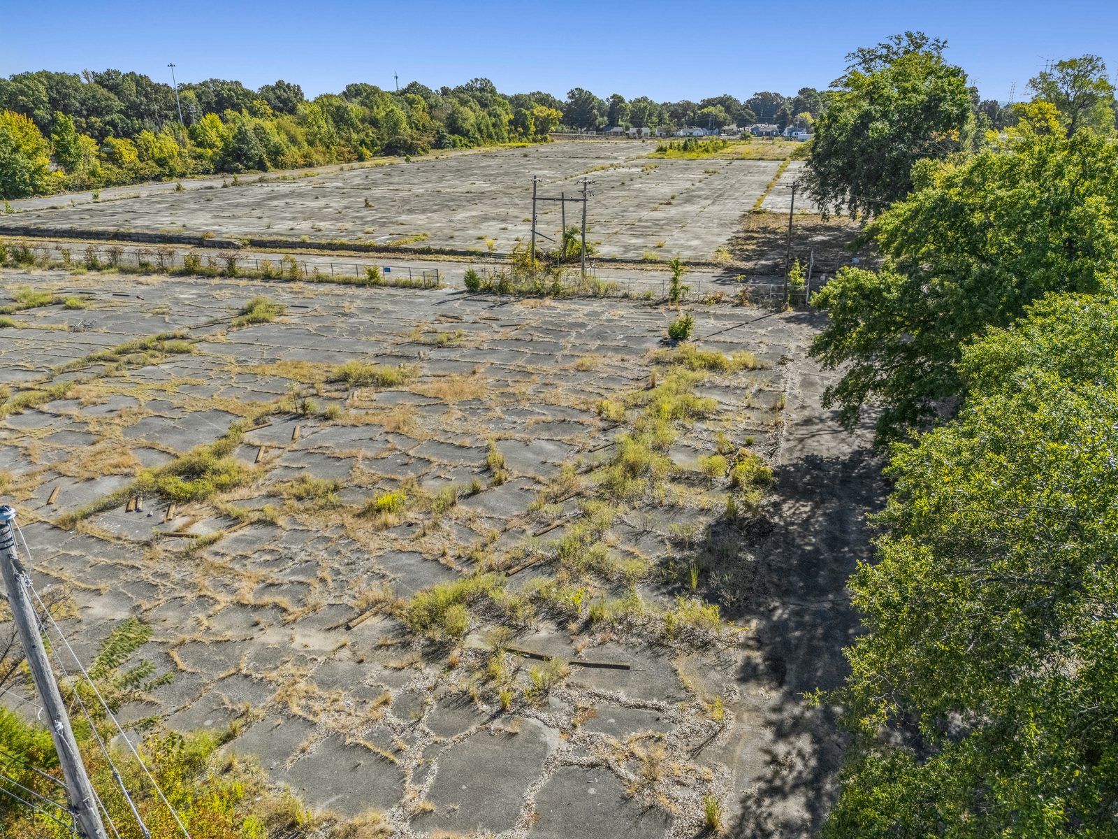 Low aerial down the length of the concrete pad, with grass growing in the joints and trees along the edge.