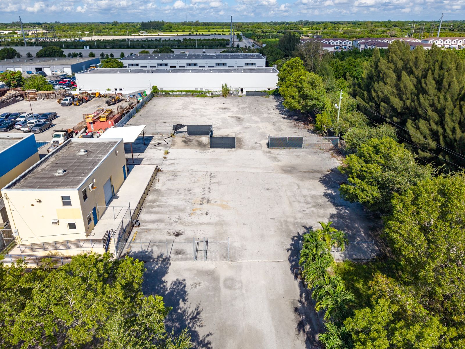 Aerial view of the paved, fenced yard stretching back from the concrete block warehouse and its raised loading dock, with trees along one side.