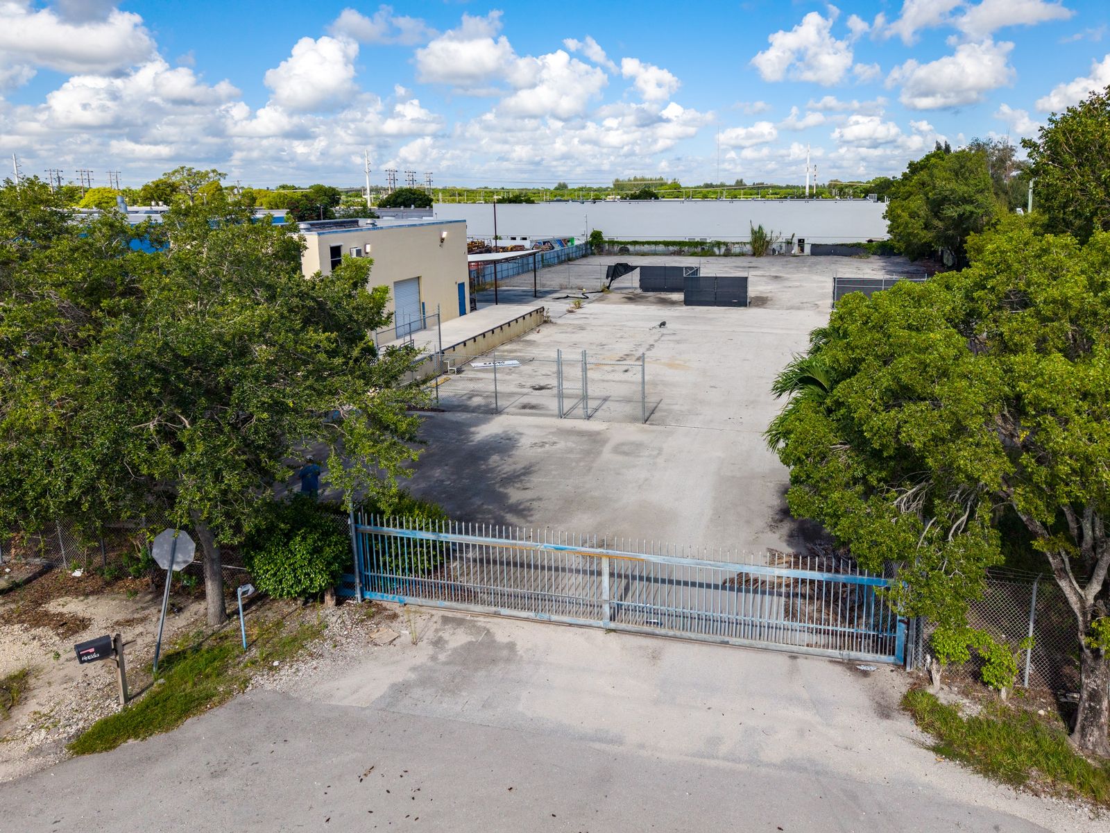 The sliding steel entry gate at the street, looking down the paved yard toward the warehouse and loading dock.