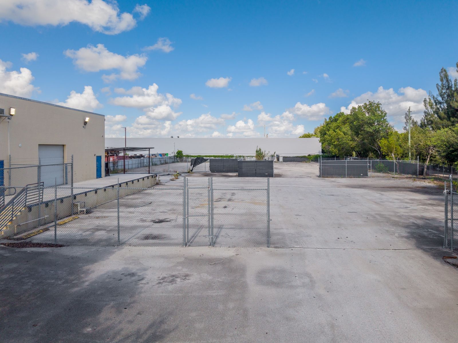 The yard seen past an interior chain link fence and gate, with the warehouse roll up door and raised dock on the left.