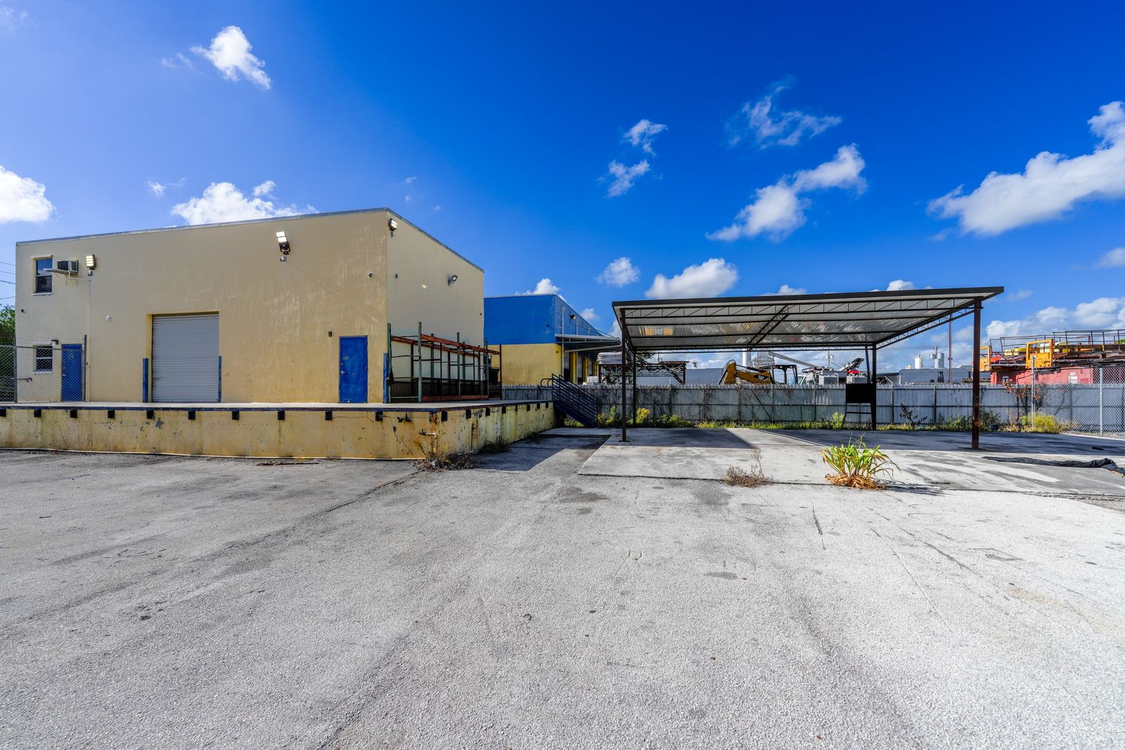 Ground level view of the warehouse roll up door at dock height, the raised loading platform and the free standing steel canopy over the paved yard.