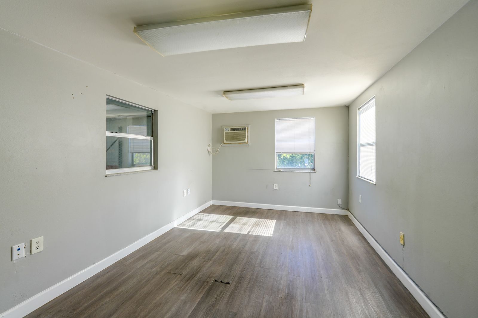 Office with plank flooring, a wall air conditioning unit, outside windows and an interior window.