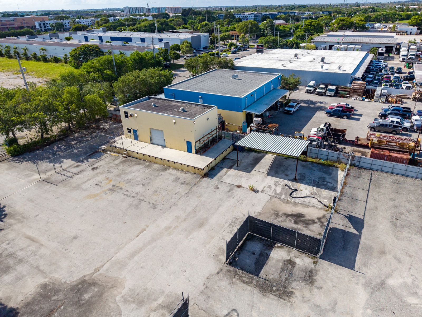Aerial view of the tan and blue building with its steel canopy, paved lot and parked vehicles, with the neighborhood beyond.