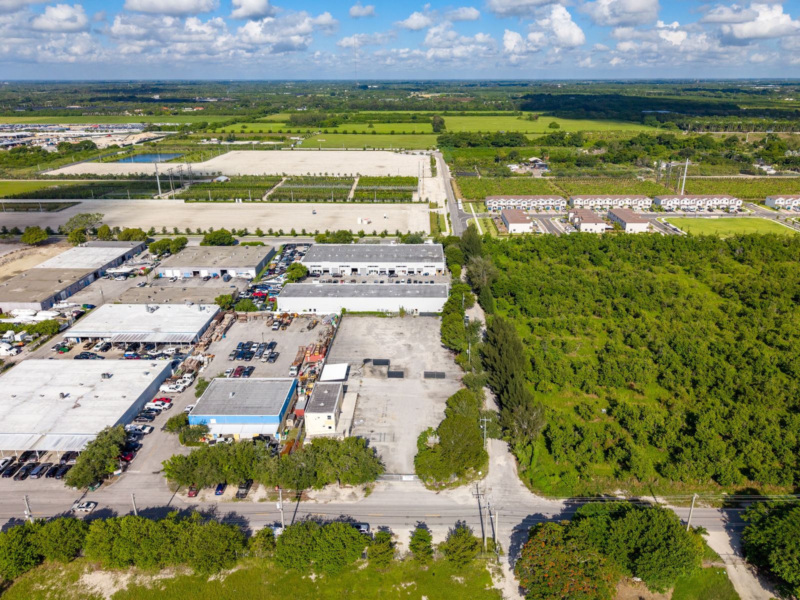 Aerial view from above the site looking toward open green space and warehouse buildings nearby.
