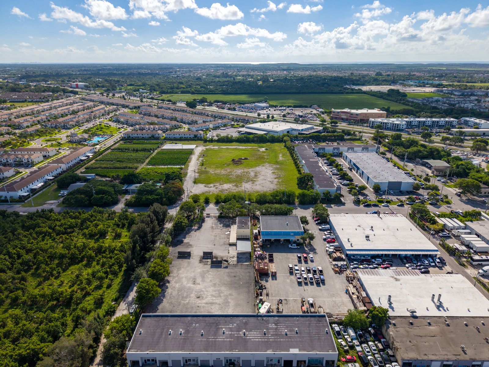 Wide aerial view from above the site looking across the neighborhood, with homes and industrial buildings in the distance.