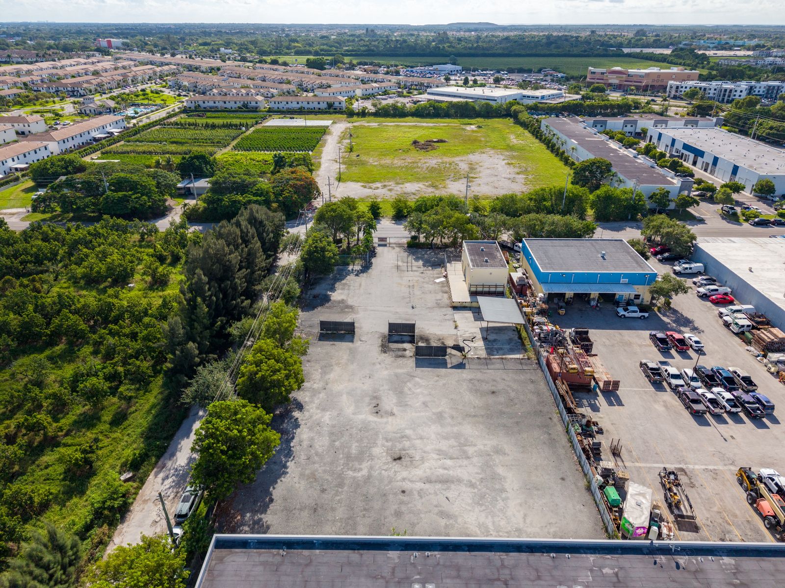 Aerial view from above the site looking toward open land, homes and warehouses in the surrounding area.