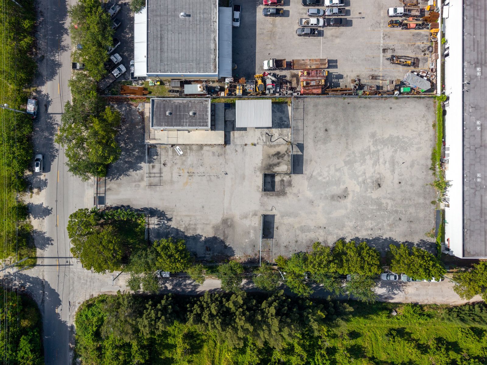 Straight down aerial of the building roof and a paved lot filled with parked vehicles and stored equipment.