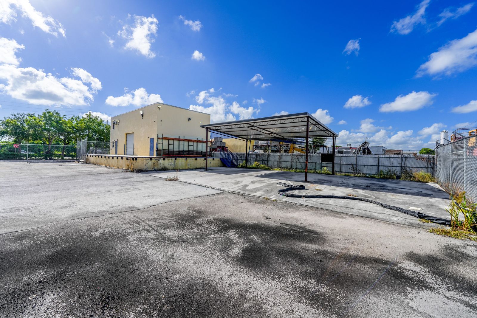 The building and its attached steel canopy, with the perimeter fence and paved yard in front.