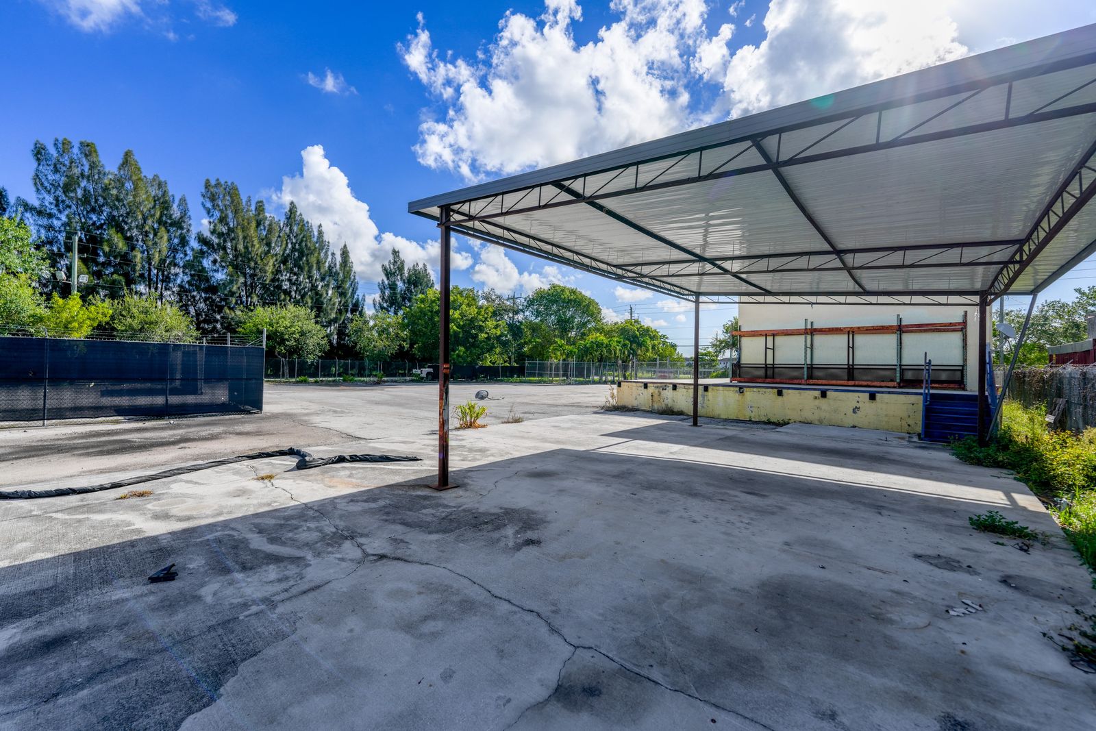 Standing under the steel canopy looking out across the paved yard, with a fenced enclosure to one side.
