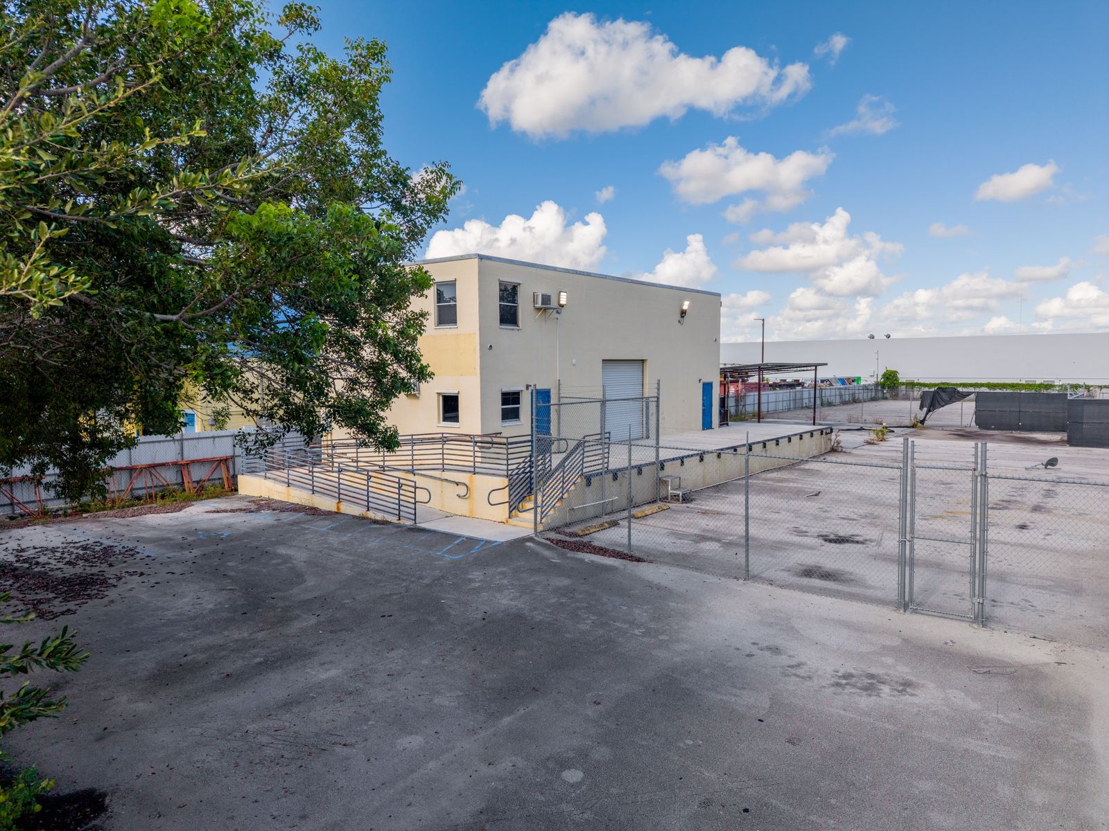 The two story office building with its entry ramp and railing, beside a gated section of the paved yard.