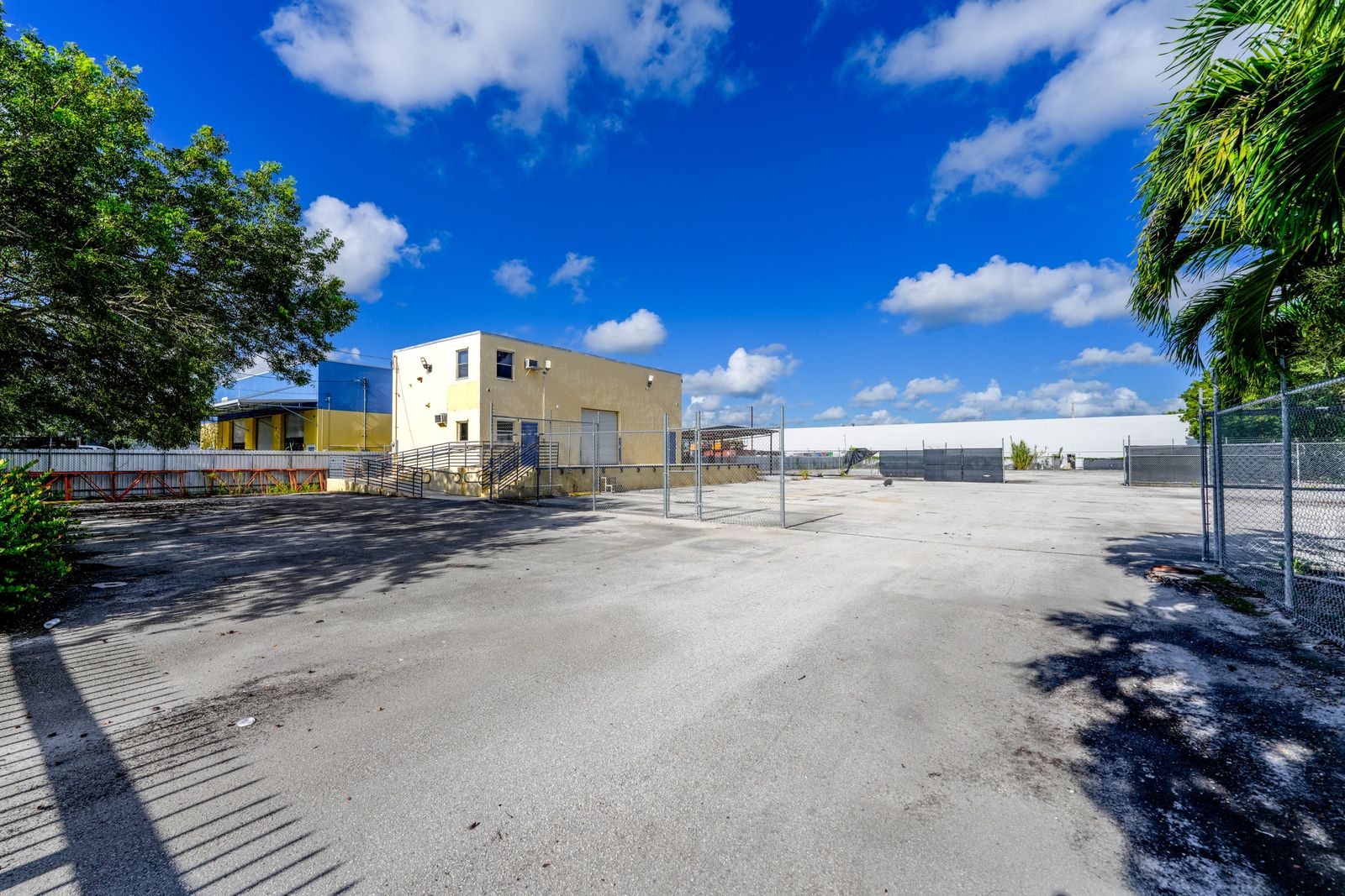 The office building beside the chain link fence, with a palm tree at the edge of the paved yard.