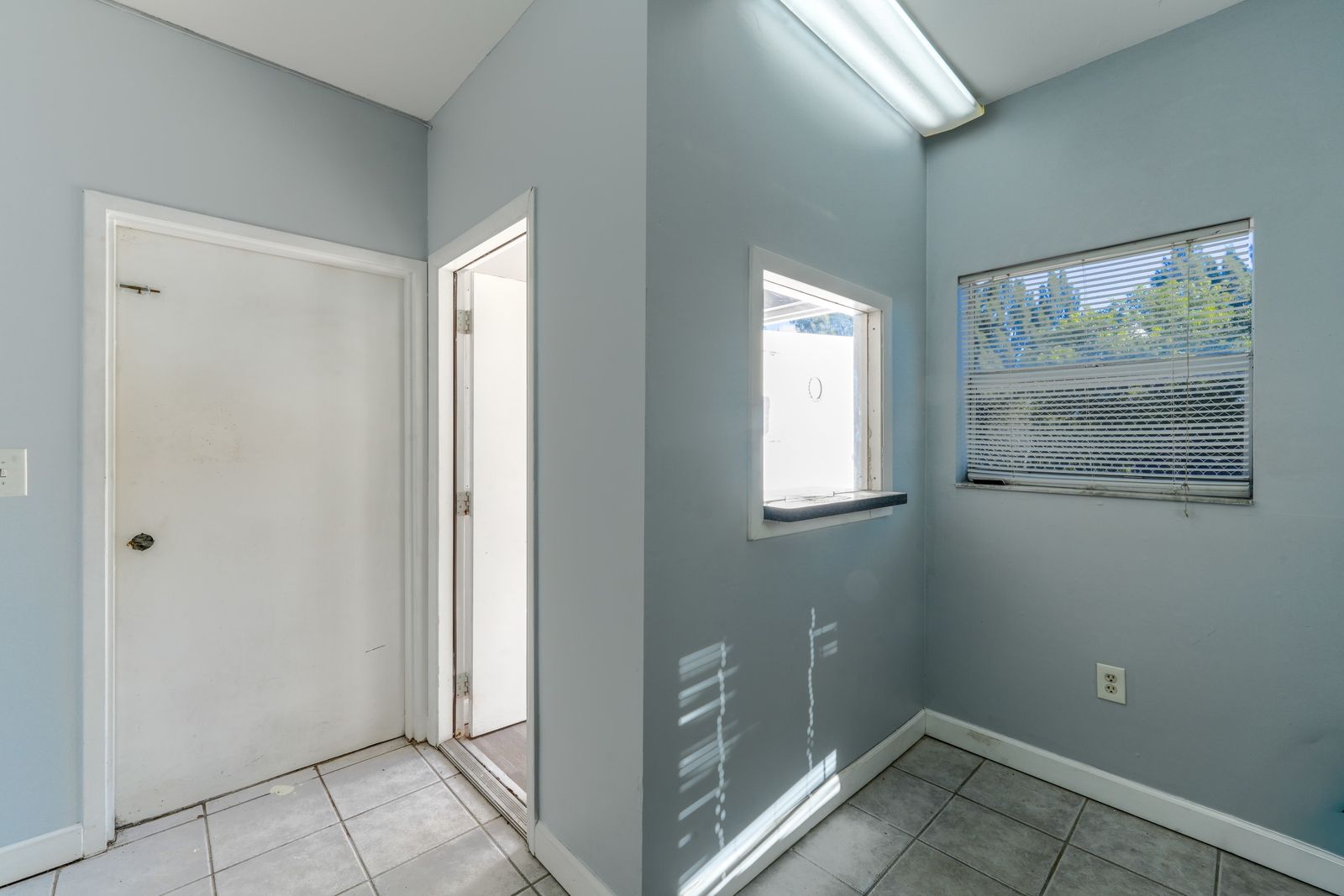 Office entry hallway with a door, a window with blinds and tile flooring.