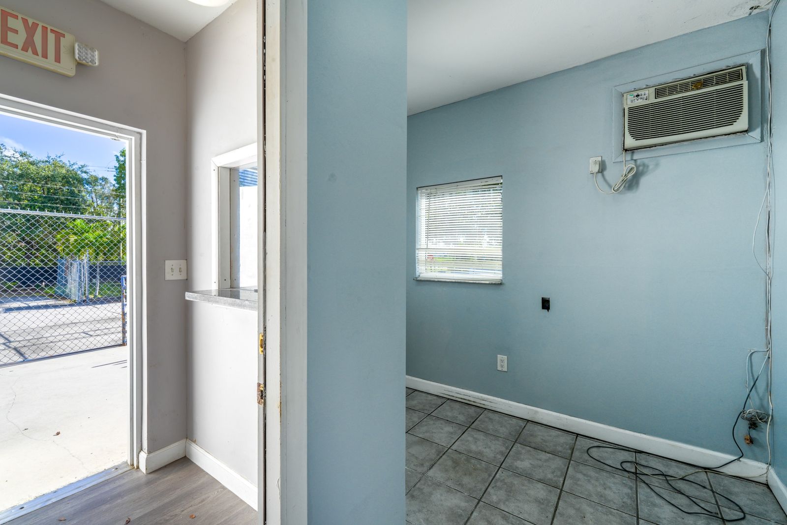 Office room with a wall air conditioning unit, a window and a door open to the yard outside.
