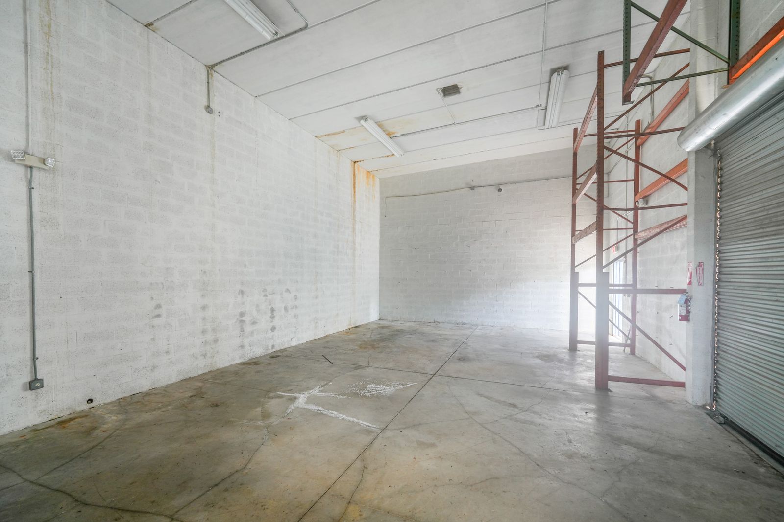 Warehouse interior with pallet racking along one wall, a roll up door and an open concrete floor.