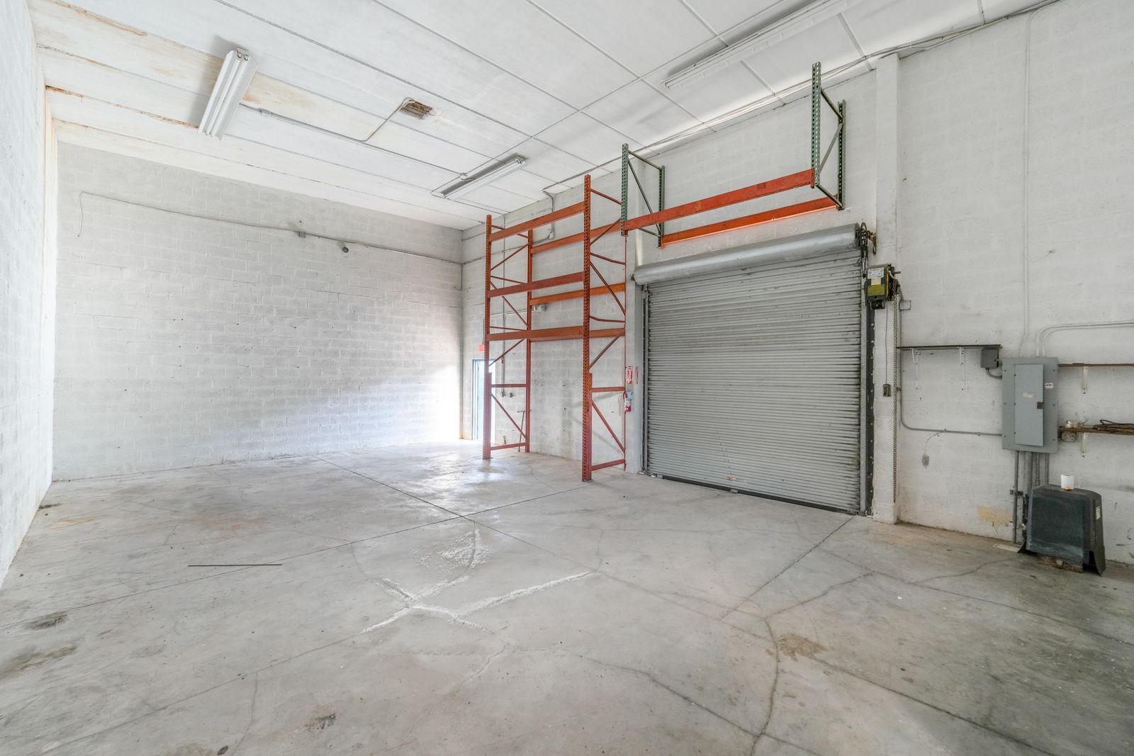Warehouse interior with orange pallet racking beside the roll up door and a concrete floor.