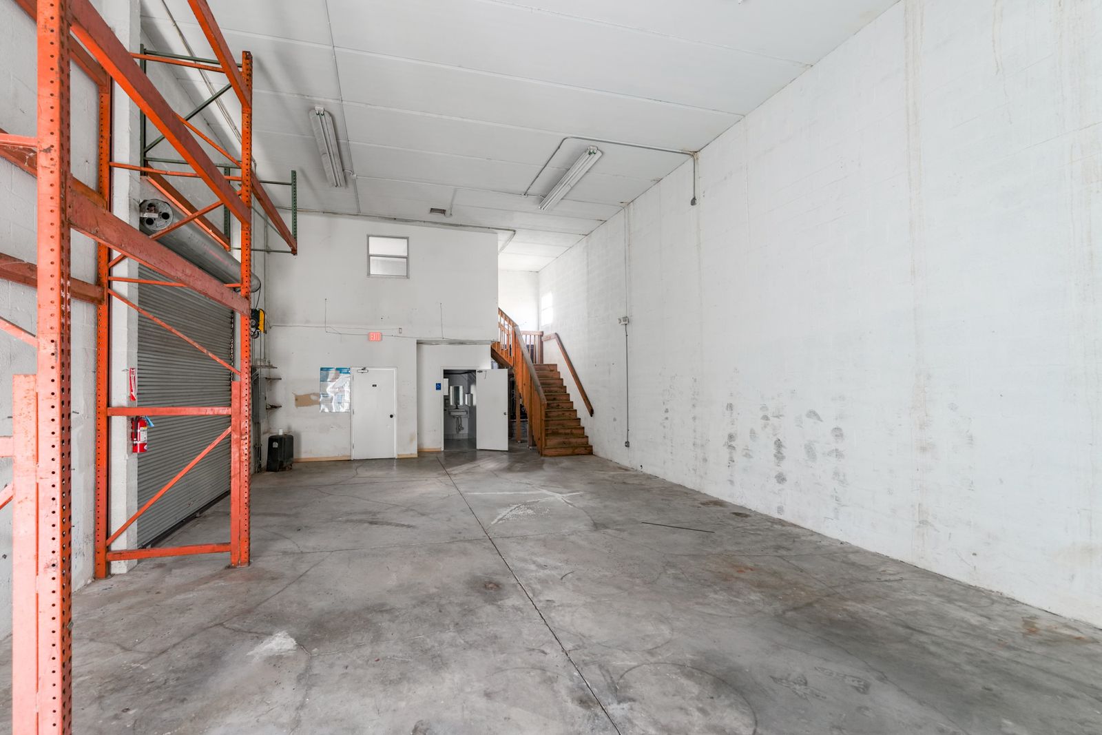 Warehouse interior with pallet racking on one side and the wooden stair to the upper level on the other.