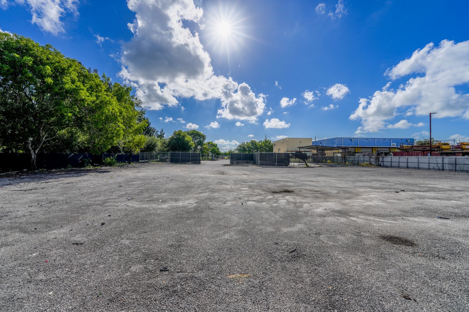 Wide view across the open paved yard, with storage bins near the fence line and a tree at the edge of the frame.