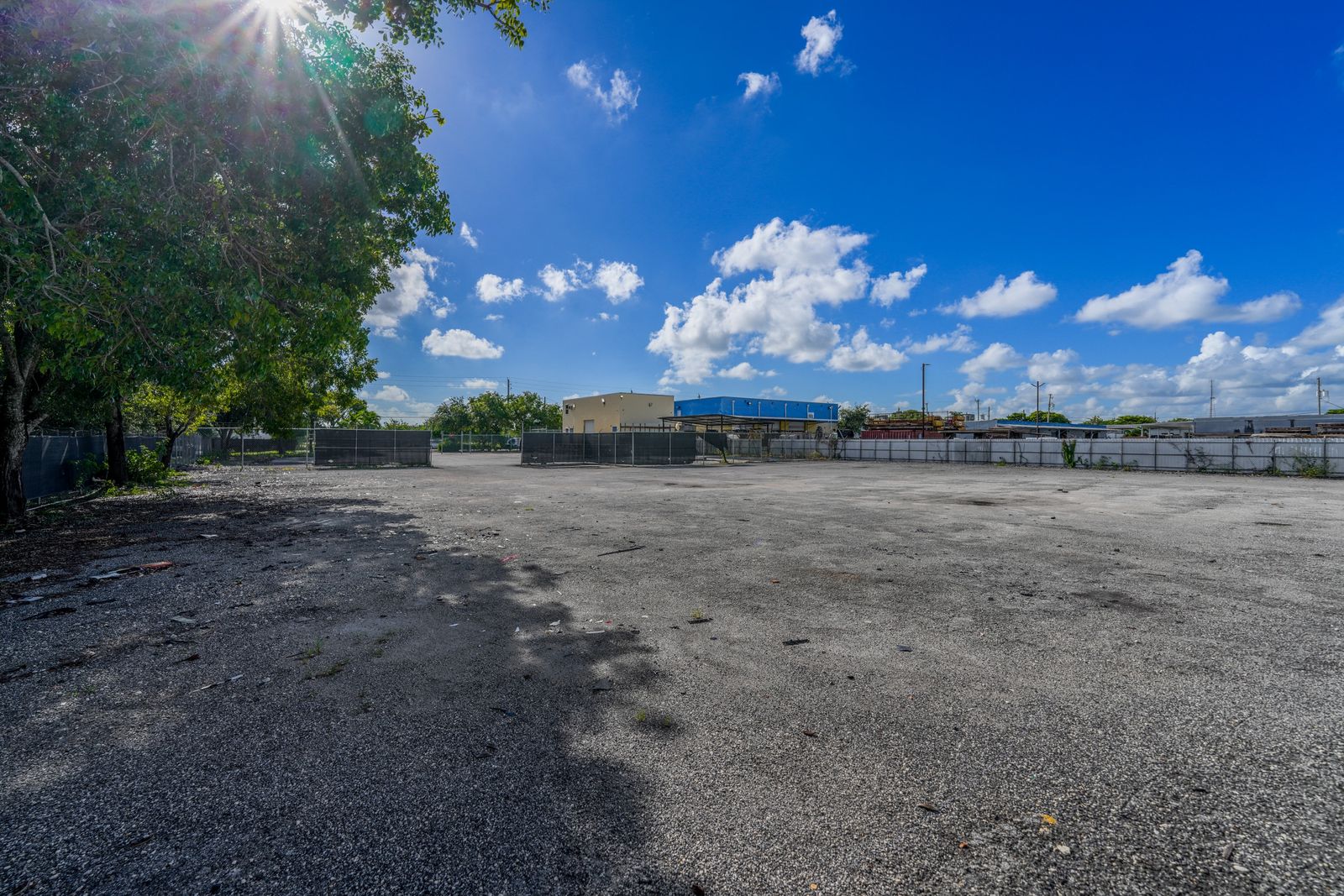 Open paved yard bordered by a fence line in the distance, with a tree overhanging one corner of the frame.