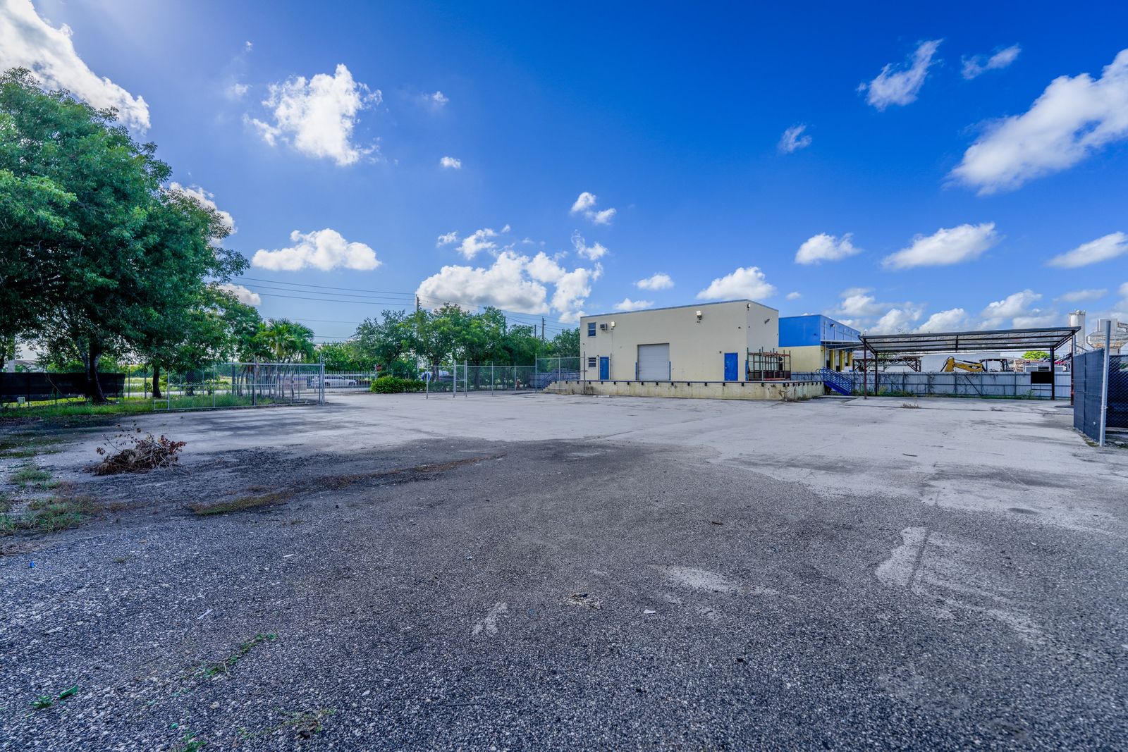 Wide open paved yard with a tree at the edge and industrial buildings visible in the distance.